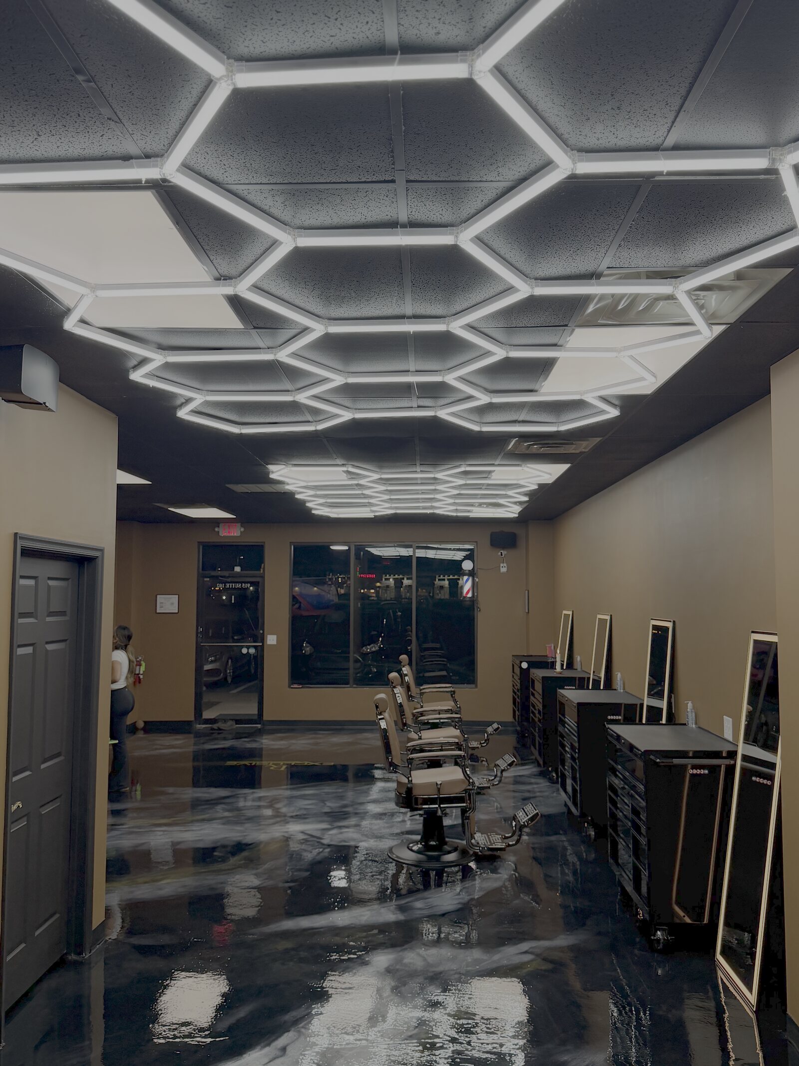 Inside Exclusive Barber Studio — hexagonal LED ceiling, marbled black epoxy floor, vintage leather barber chairs and the storefront beyond.